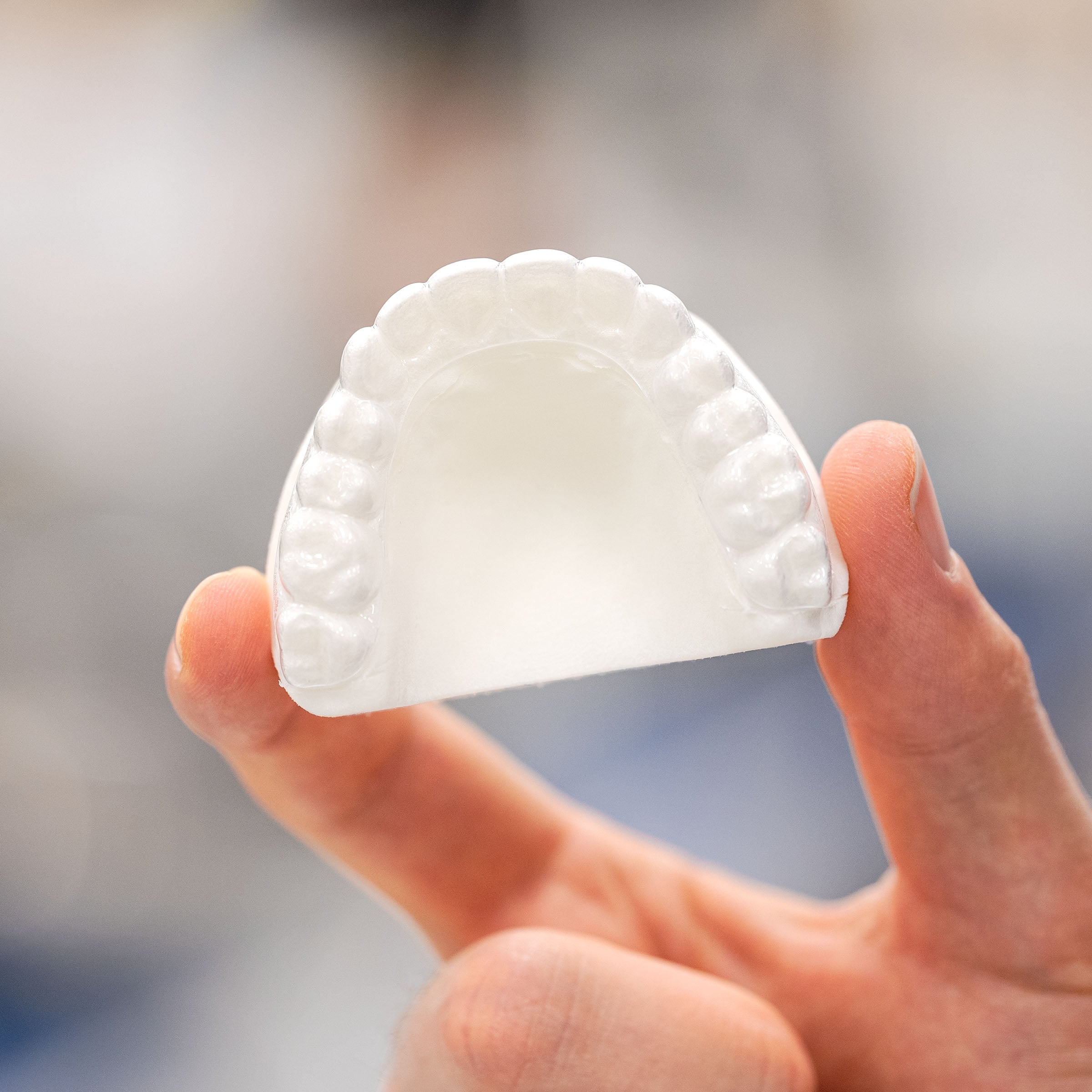 Invisacryl T™ TPU Material aligner appliance on model held over abstract blurred out background