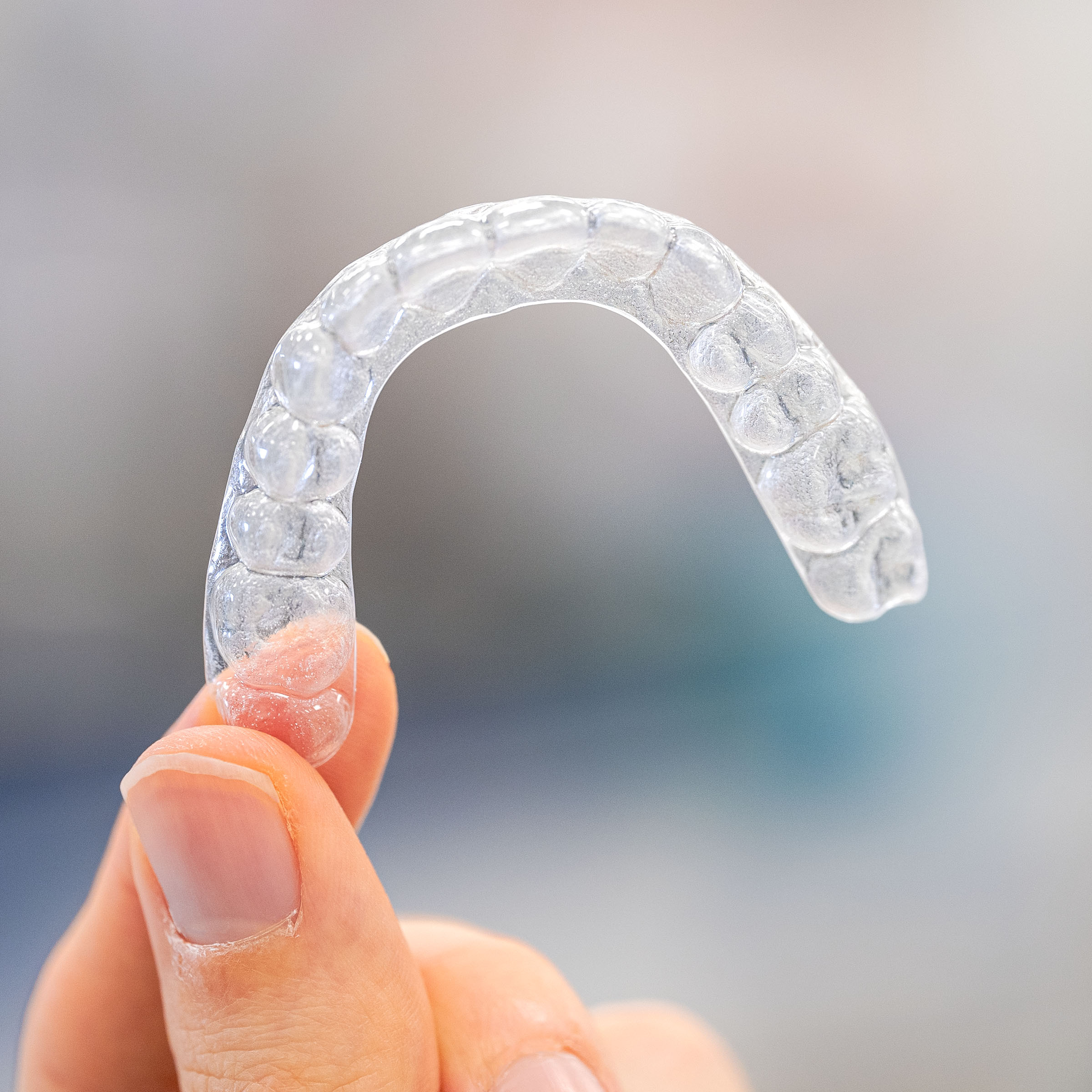 Invisacryl T™ TPU Material aligner appliance held over abstract blurred out background