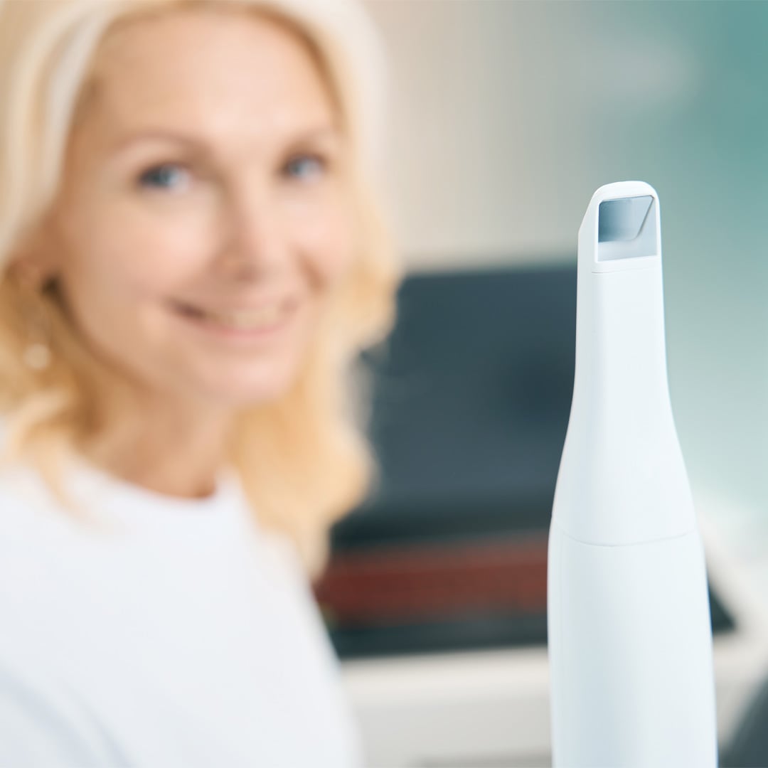 Female dental professional holding digital scanner in dental office with laptop in background