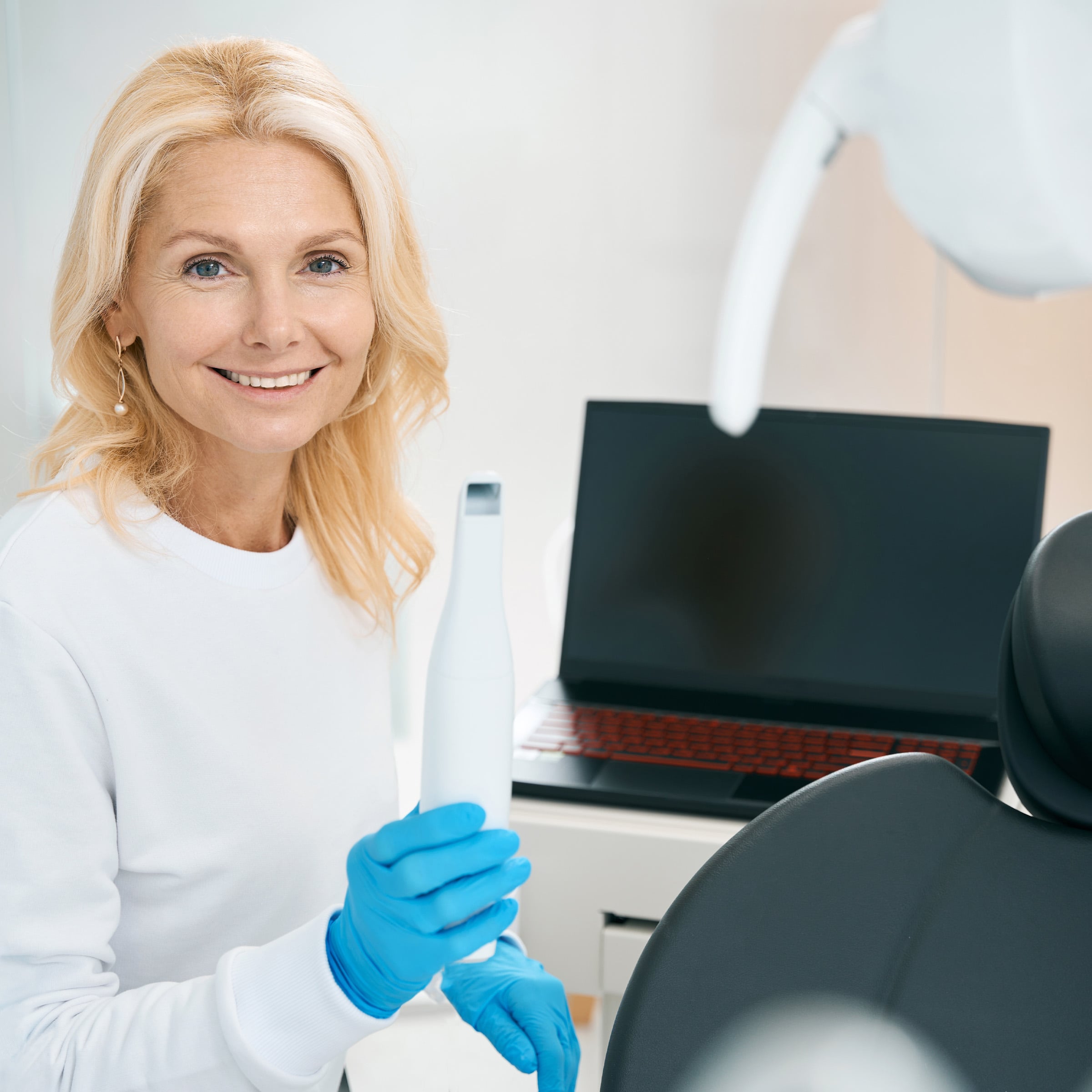 Female dental professional holding digital scanner in dental office with laptop in background